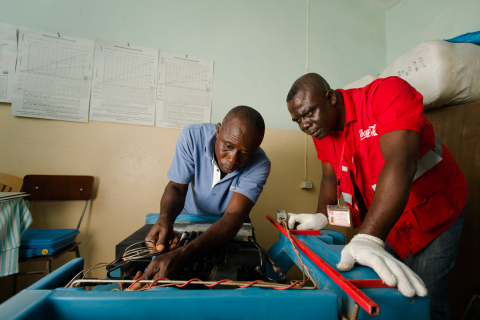可口可乐公司冷藏装置技师Maxwell Ayisi（右）和加纳健康服务冷藏技师Livingstone Modey（左）在加纳沃尔特地区佩吉迪扎克的一家诊所修理用于储存疫苗的气电双动力冷藏装置（照片：美国商业资讯）。